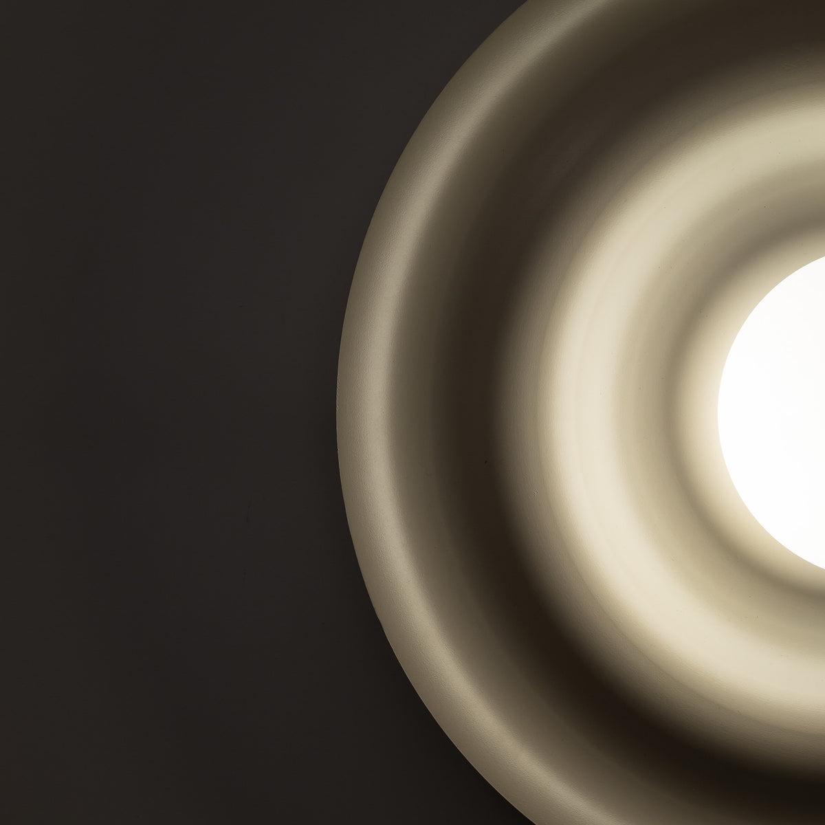 ONDA wall sconce lit, warm light from the opal shade spreading across the matte steel disc